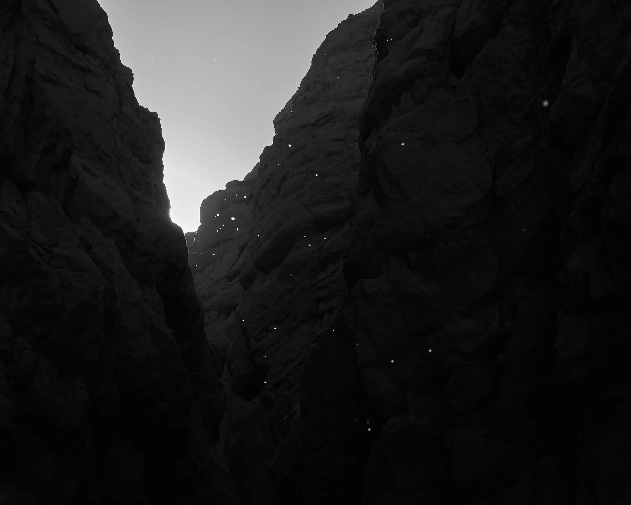 Black and white shot of gnats glowing like stars in a narrow slot canyon.