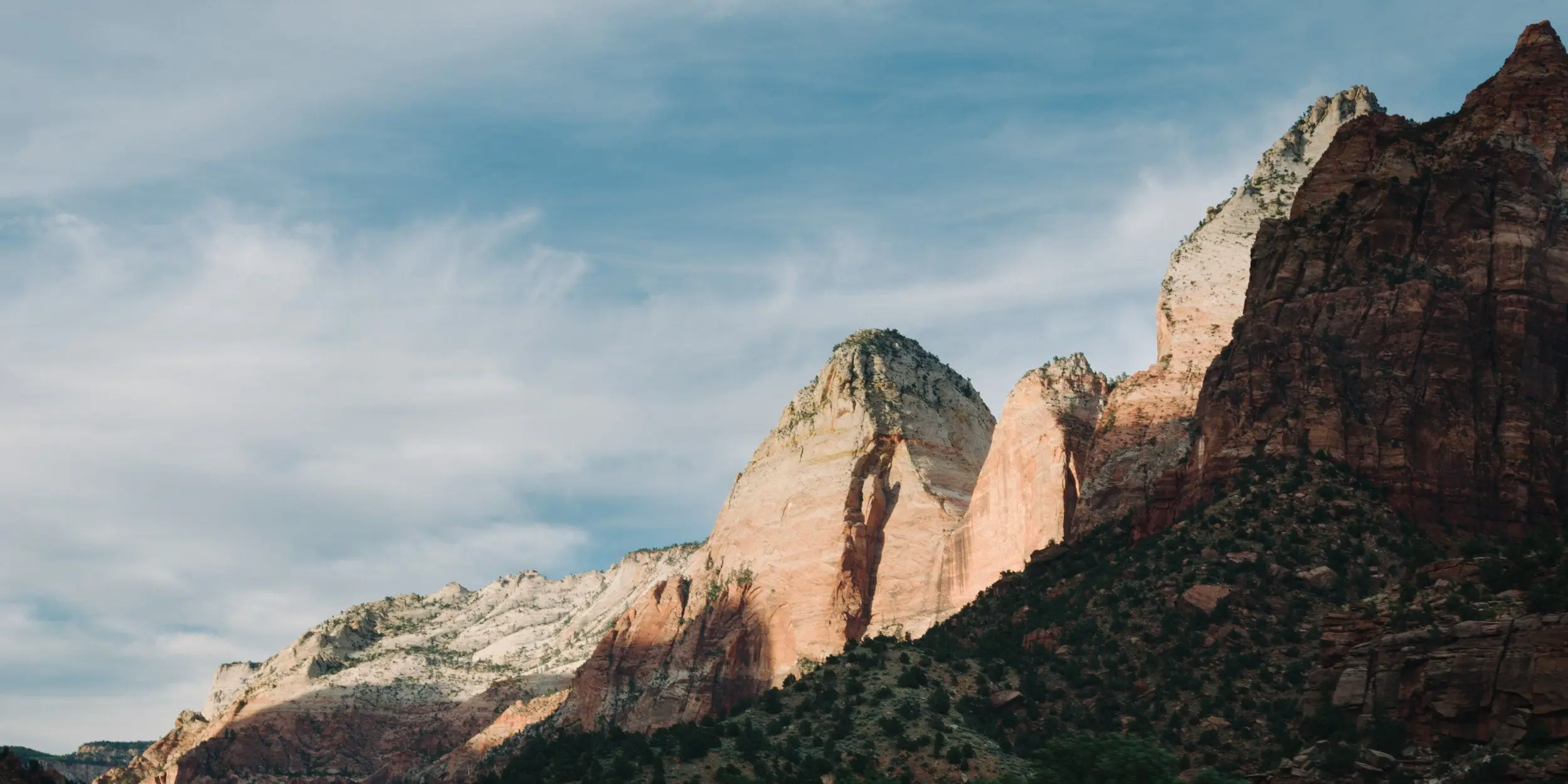 Mountains under wispy clouds through the Zion – Mount Carmel Highway at sunset.